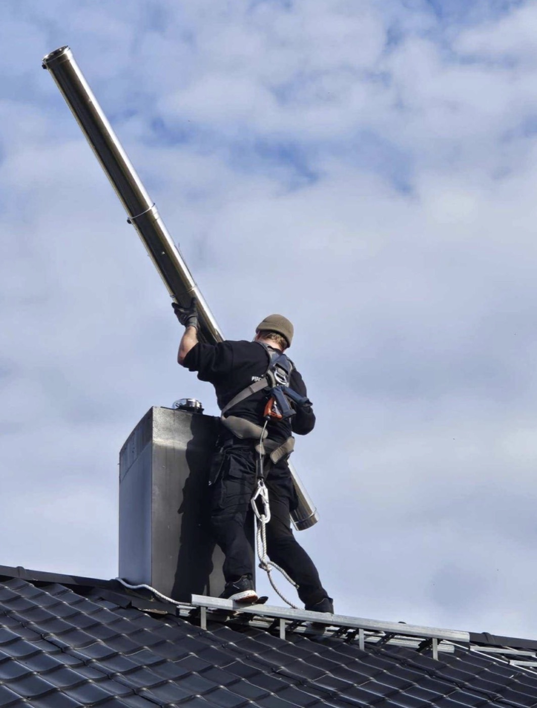 Montør hever foring av stålpipe ned i pipeløpet på tak på Østre Tromøyvei, Kongshavn